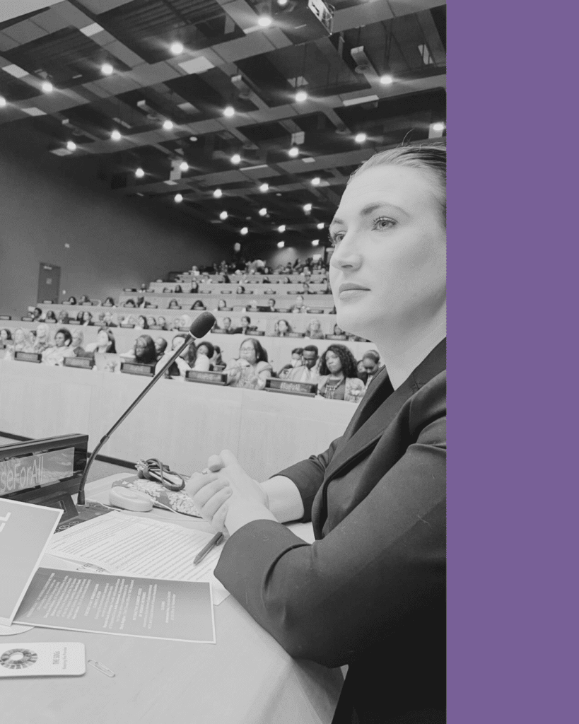 Imagen en blanco y negro con Anastasia Holoboff, integrante del equipo WEI. Se encuentra sentada frente a un micrófono en un salón de conferencias con otras personas en la audiencia. Del lado derecho de la imagen hay una barra deccorativa de color morado.
